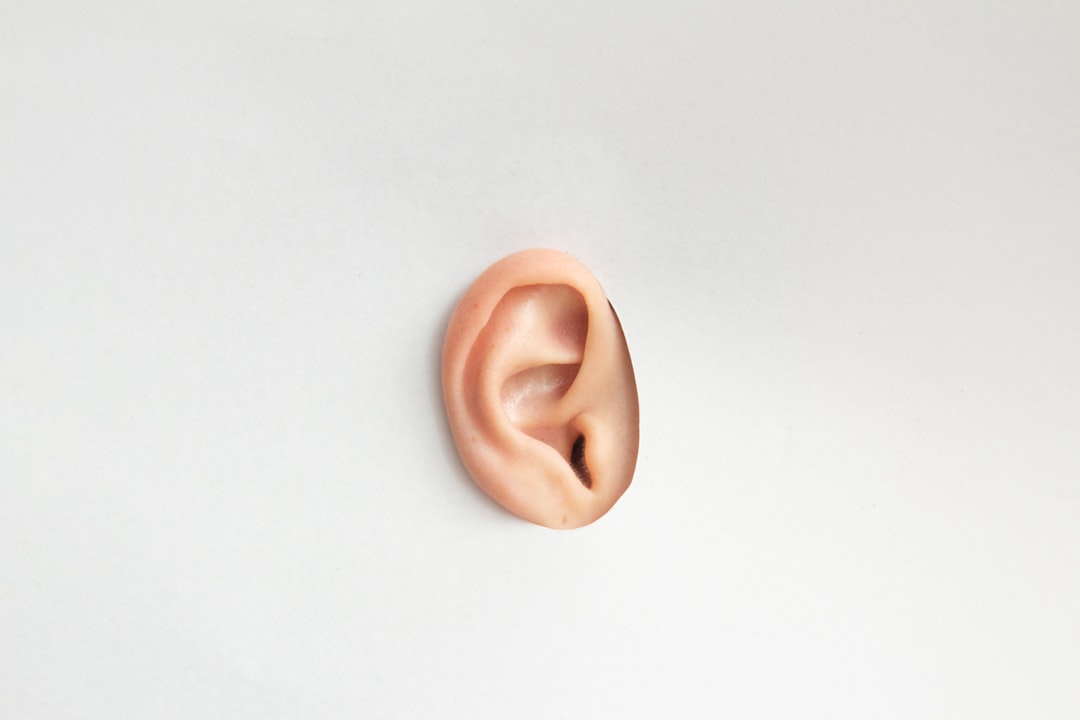 A close-up of a person gently cleaning their ear with a cotton swab, surrounded by ear care products like drops and a soft towel.
